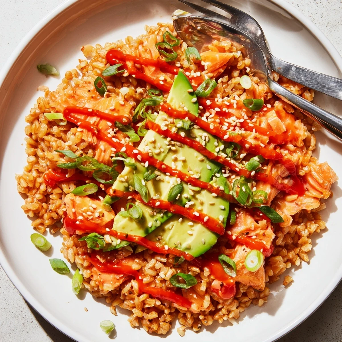 Flaked salmon and creamy avocado top seasoned rice in this Emily Mariko Salmon Rice Bowl, drizzled with spicy mayo and served with nori sheets.