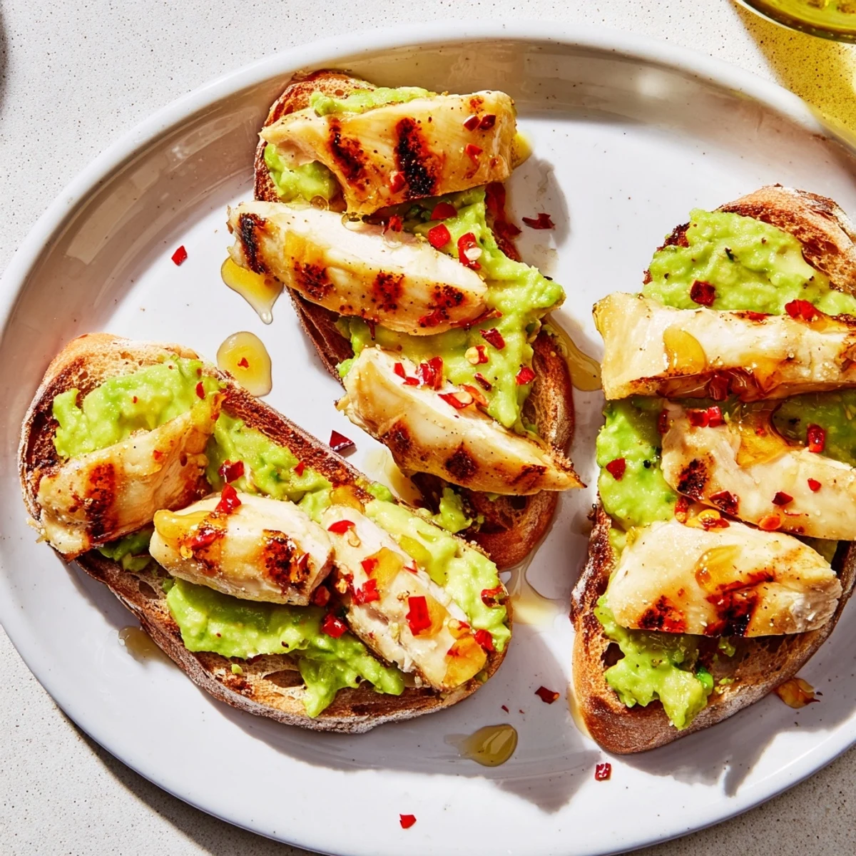 A close-up of vibrant smashed avocado chicken toast, garnished with fresh herbs and a drizzle of honey on crispy bread.
