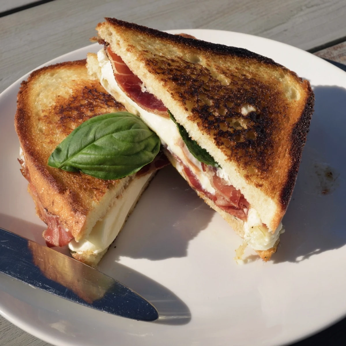 A close-up of melted burrata and crisp prosciutto inside a buttery, golden-grilled cheese sandwich.  