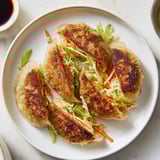 Four crispy rice paper dumplings pan-fried to perfection, showing a crunchy golden texture next to a vibrant dipping sauce with chili flakes and scallions.  