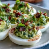 Vibrant guacamole-stuffed deviled eggs topped with smoked paprika and diced tomatoes.  