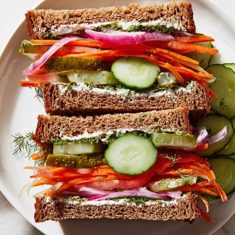 Image: a beautifully stacked, delicious crunchy dill pickle sandwich filled with fresh vegetables and creamy spread.