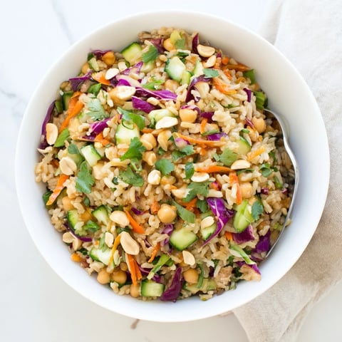A vibrant Peanut Chickpea Rice Bowl topped with crunchy peanuts and colorful shredded vegetables.  
