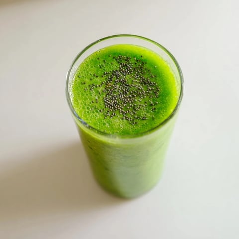 Tall glasses of vibrant Green Detox Smoothie filled with ice-cold, bright green liquid and dotted with chia seeds next to fresh produce.