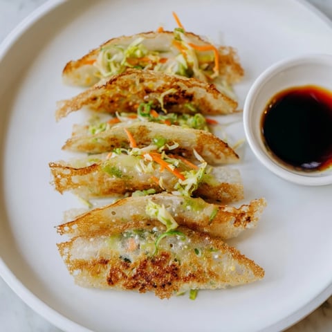 Golden-brown crispy rice paper dumplings stacked on a white plate with a small bowl of tangy dipping sauce, garnished with fresh cilantro and sesame seeds.  