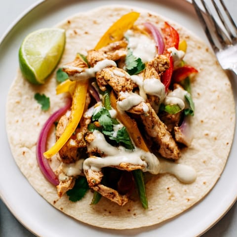 Golden, juicy Chicken Fajitas recipe filling with peppers, onions, and tangy lime-cilantro crema.