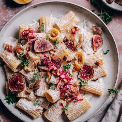 A close-up shot of the Pasta with Roasted Grapes, garnished with fresh herbs and pine nuts.