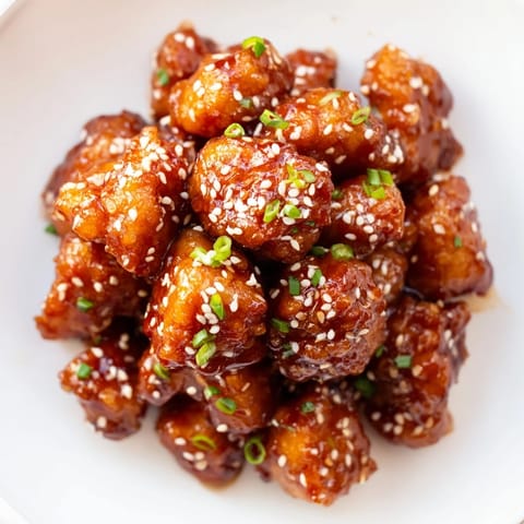 A close-up shot of golden Honey-Sriracha Chicken Bites, with sesame seeds and chives garnishing the dish.