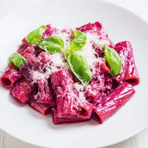 Fresh basil and grated Parmesan garnish this Pink Pasta with Beet Cream, served alongside a glass of white wine.