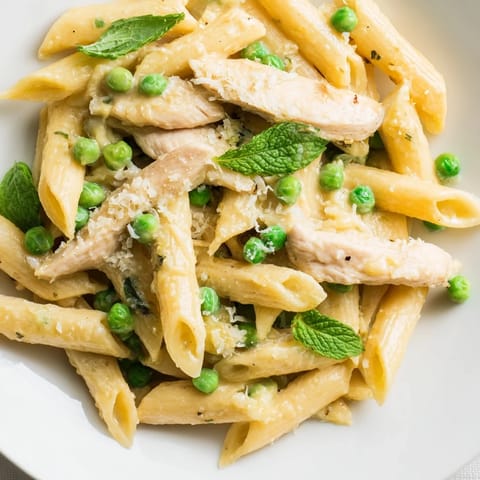 Fork-ready plate of Pea & Mint Chicken Pasta topped with grated Parmesan and herbs, served alongside a crisp salad.