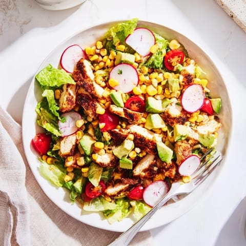 Colorful bowl of Roasted Corn & Chicken Chopped Salad with romaine, cherry tomatoes, and zesty lime dressing garnished with cilantro.
