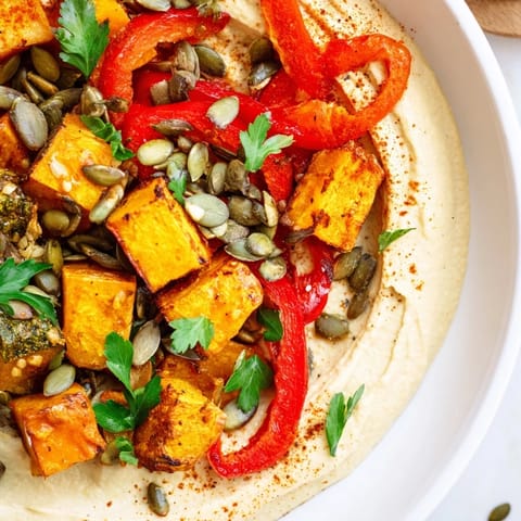 A hearty scoop of this Roast Squash and Hummus Winter Salad reveals vibrant orange and red vegetables over smooth hummus, finished with smoky paprika.  