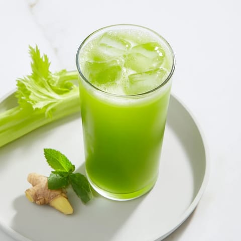 Tall pitcher of vibrant green Celery Ginger Lemon Juice next to crisp celery sticks and lemon wedges on a clean kitchen counter.