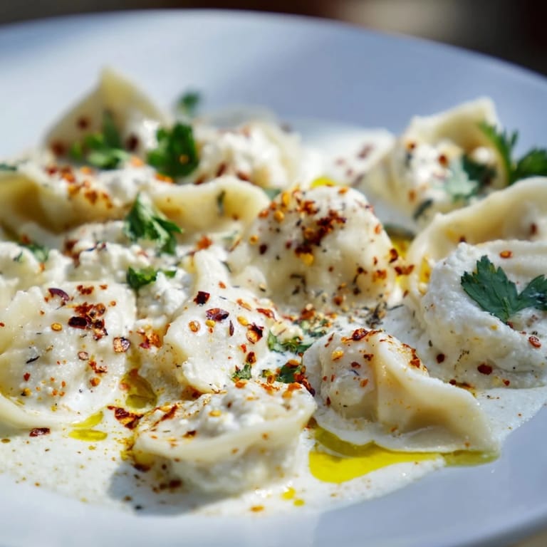 A close-up of perfectly formed Turkish cheesy manti, topped with a vibrant spiced butter sauce.
