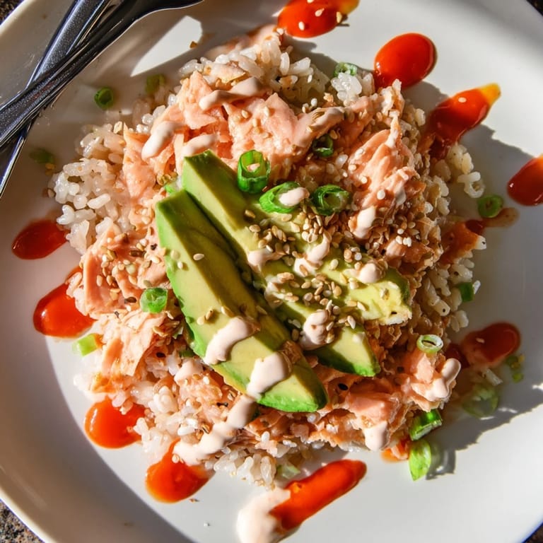 A close-up of the vibrant Emily Mariko Salmon Rice Bowl reveals fluffy rice, tender salmon, avocado slices, and a drizzle of spicy mayo.