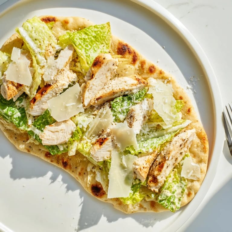 A close-up of Chicken Caesar Flatbread topped with shaved parmesan and halved cherry tomatoes.