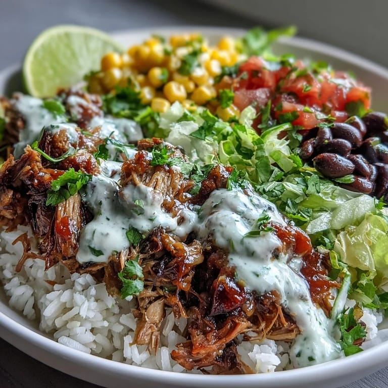 Steaming Carnitas Burrito Bowl featuring shredded pork, cilantro-lime rice, and a drizzle of tangy lime crema garnish.