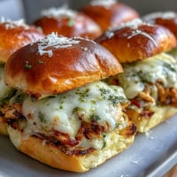 Golden-brown Pesto Chicken Parmesan Sliders on a platter, showcasing melty mozzarella and vibrant green pesto on fluffy brioche buns.